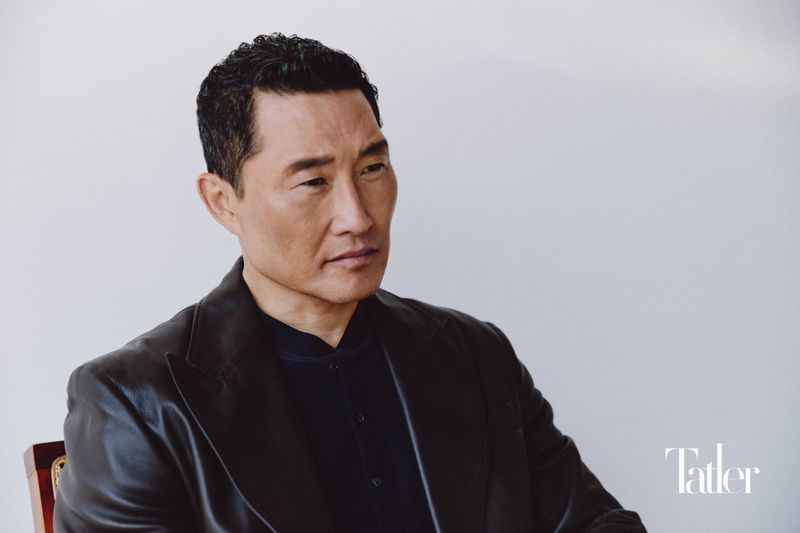 Portrait of actor Daniel Dae Kim wearing a dark leather jacket and dark shirt against a white wall for Tatler Asia.