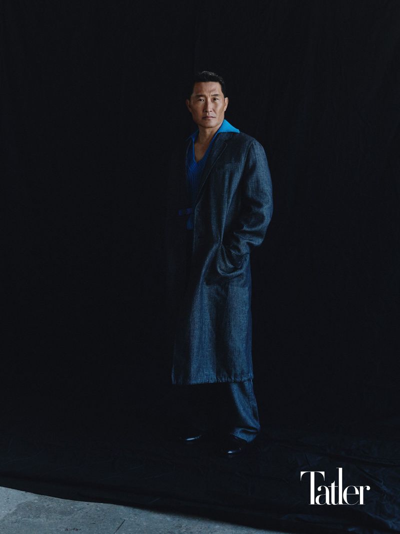 Actor Daniel Dae Kim poses in a long denim coat over a royal blue shirt against a dark studio backdrop for Tatler.