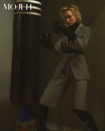 Blonde woman wearing a grey suit and black boxing gloves throwing a punch next to a punching bag for Mojeh Magazine