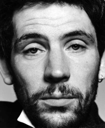 Black and white tight close-up portrait of actor Josh O'Connor looking directly into the camera with a subtle, serious expression.