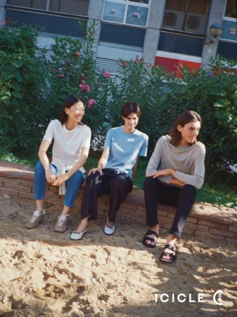 Three models seated together on a low brick wall outdoors wearing casual t-shirts and trousers for ICICLE SS26 B Line.