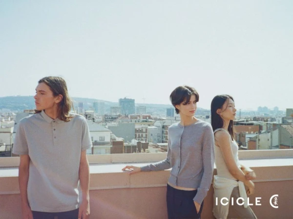 Three fashion models in neutral knitwear and polo shirts posing on an urban rooftop overlooking a cityscape.