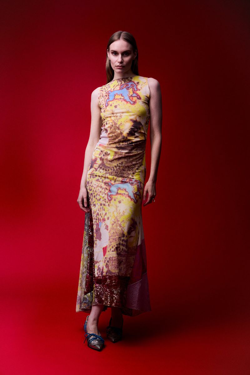 Model posing in a printed sleeveless maxi dress against a rich red seamless backdrop.