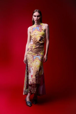 Model posing in a printed sleeveless maxi dress against a rich red seamless backdrop.