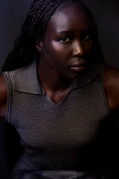 Black female model with braided hair wearing a textured grey sleeveless knit polo in soft low-key studio lighting.
