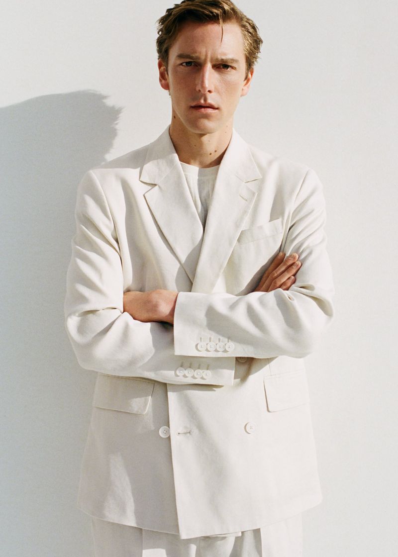 Model Quentin Demeester wearing an off-white double-breasted suit with arms crossed against a white studio background.