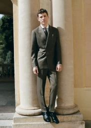 Model George Barnett wearing an olive double-breasted suit leaning against a stone column for Mango.