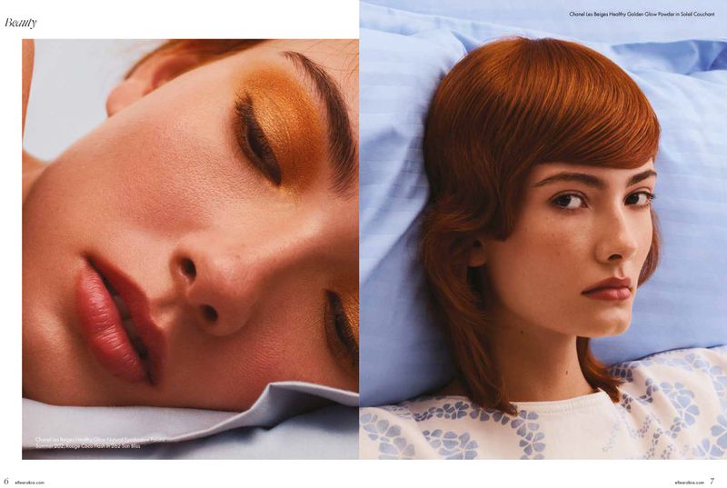 Close-up fashion editorial shot featuring a red-haired model with striking eye makeup lying on a bed with light blue linen.