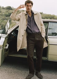 Model Pierre-Benoit Talbourdet in a beige trench coat and brown trousers standing by an open vintage car door.
