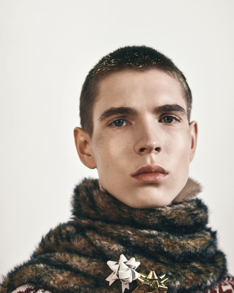 Male model wearing a faux fur neck wrap pinned with gift bows against a white background for Oscar Ouyang AW26.