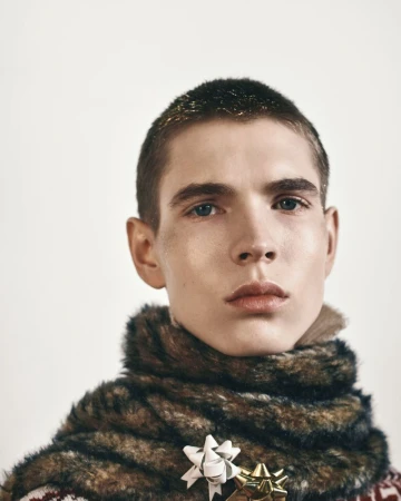 Male model wearing a faux fur neck wrap pinned with gift bows against a white background for Oscar Ouyang AW26.
