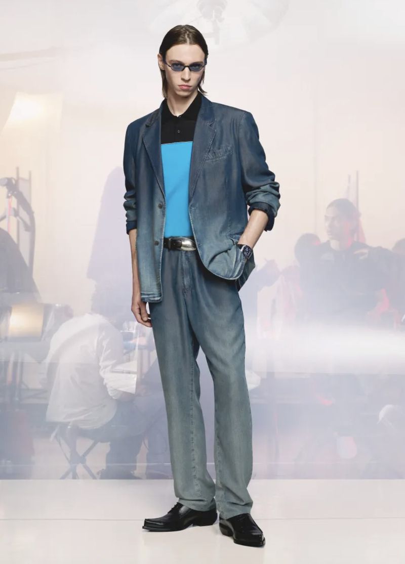 Model wearing a washed denim blazer with matching jeans, dark sunglasses, and black dress shoes in a studio setting.