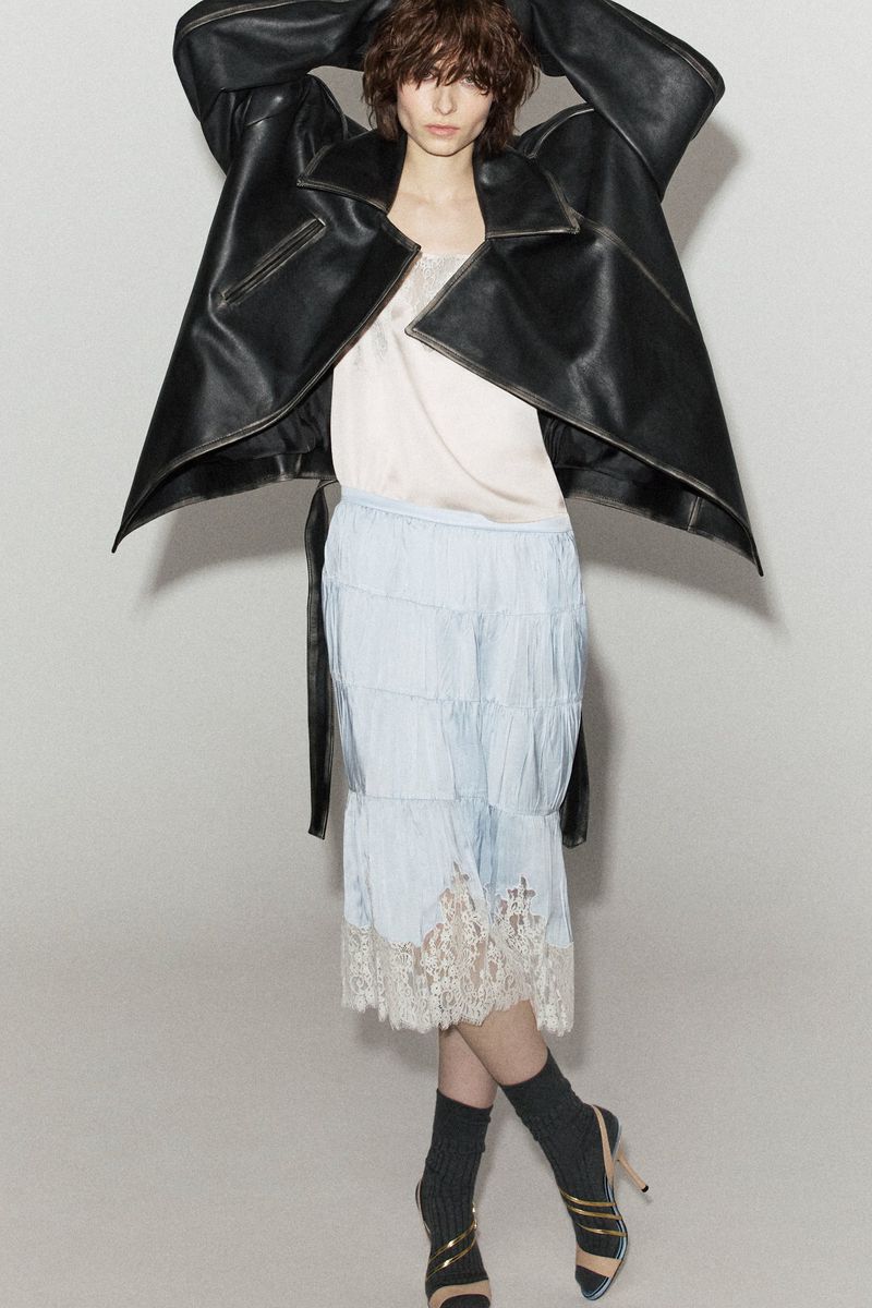 Evie Nopere wearing an oversized black leather jacket and a tiered lace-hem skirt against a grey studio backdrop for N21.