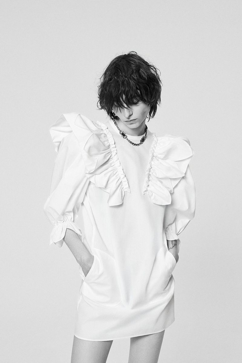 Model wearing a white ruffled dress with hands in pockets against a plain grey backdrop in N21 Resort 27 project.