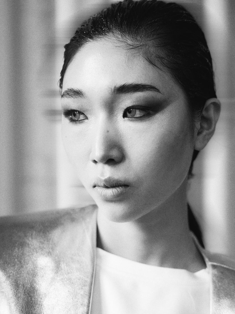 Monochrome close-up portrait of an East Asian woman with slicked hair and smoky eye makeup wearing a metallic jacket.
