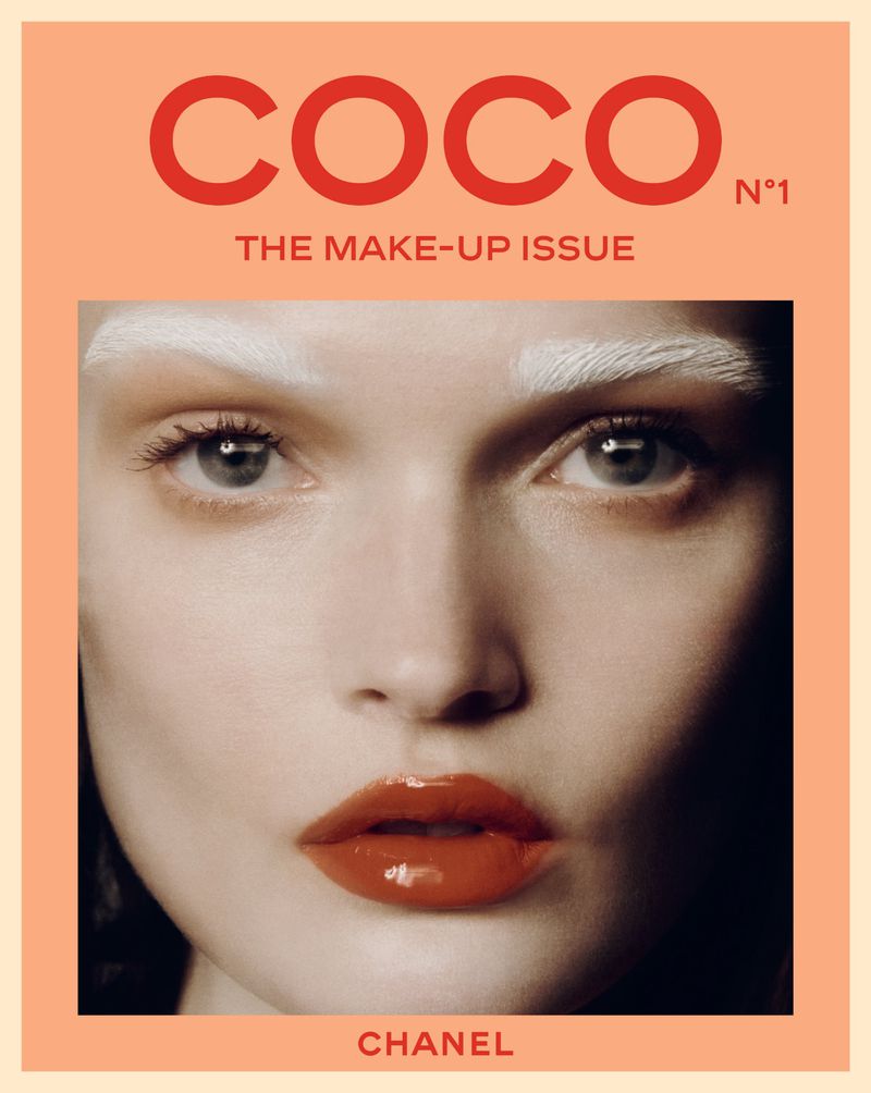 Close-up portrait of a woman with white painted eyebrows and glossy orange-red lipstick on the cover of Chanel Coco Magazine.