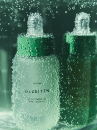 Two Gezeiten skincare serum dropper bottles submerged in water and covered in effervescent bubbles against a green backdrop.
