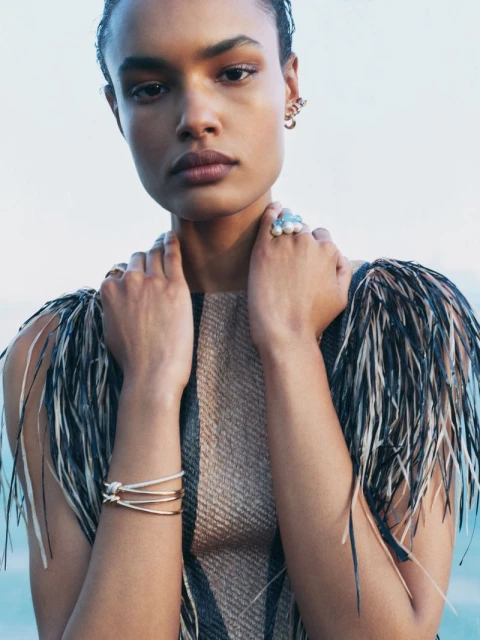 Model Ana Beatriz Cortes wearing fine jewellery and feathered apparel against an outdoor sky background