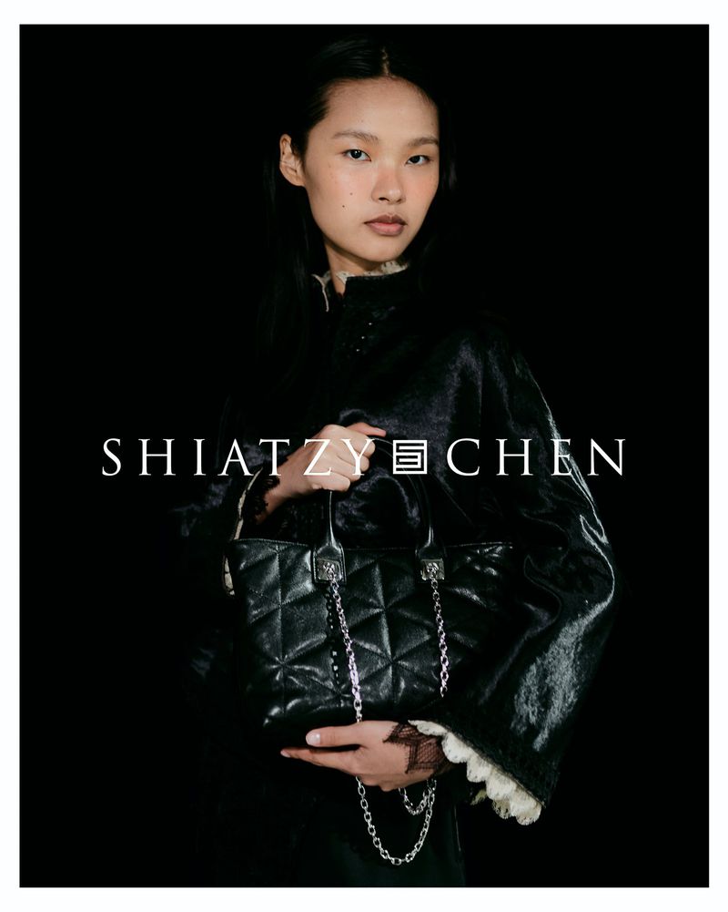 Model holding a quilted black leather handbag with a silver chain strap against a black background for Shiatzy Chen.