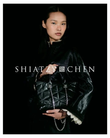 Model holding a quilted black leather handbag with a silver chain strap against a black background for Shiatzy Chen.