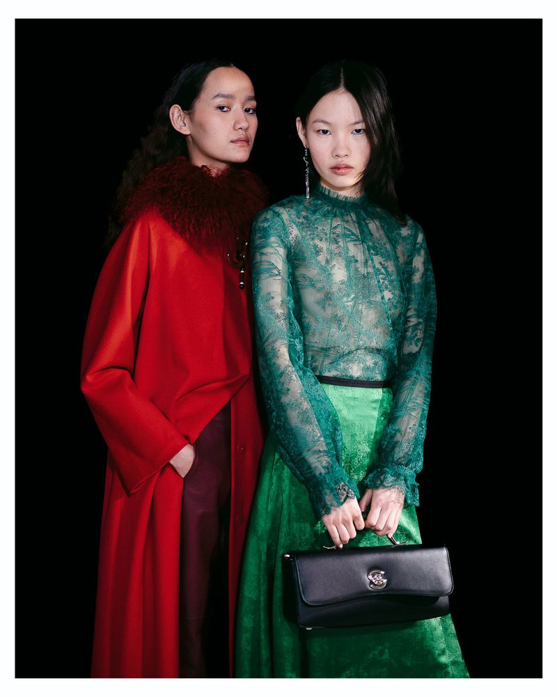 Two models pose in Shiatzy Chen designs, one in a green lace blouse holding a black clutch and the other in a vibrant red coat.