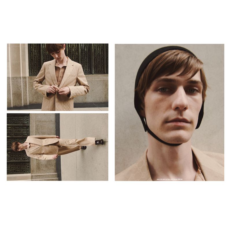 Fashion editorial with a young male model wearing a tan suit and black swim cap against an urban backdrop on an overcast day.