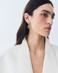 Woman wearing diamond drop earrings and layered delicate pendant necklaces styled with an open white blazer.