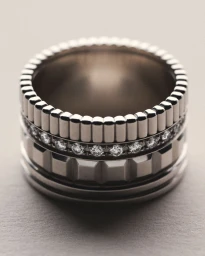Macro shot of a stacked silver wedding band with diamond pave and geometric ridges on a neutral textured surface.