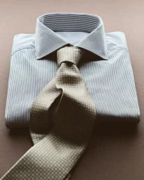 Folded pinstriped dress shirt paired with a knotted beige patterned tie against a neutral background.