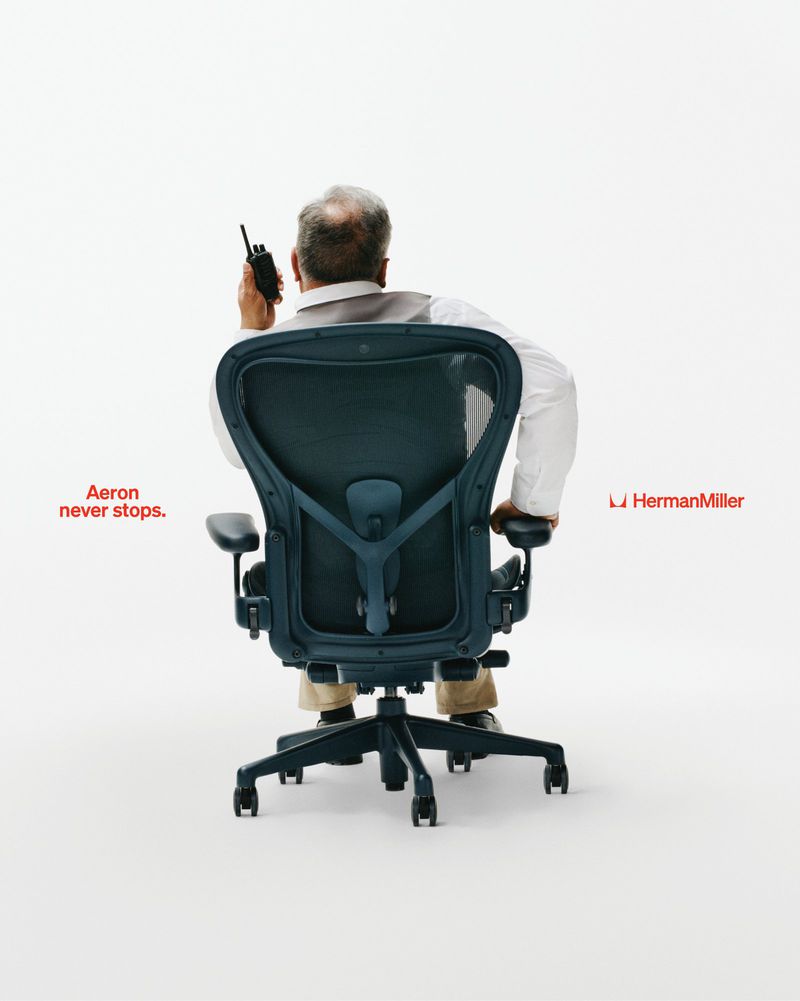 Man seen from behind sitting in an ergonomic office chair holding a walkie-talkie against a white studio background.