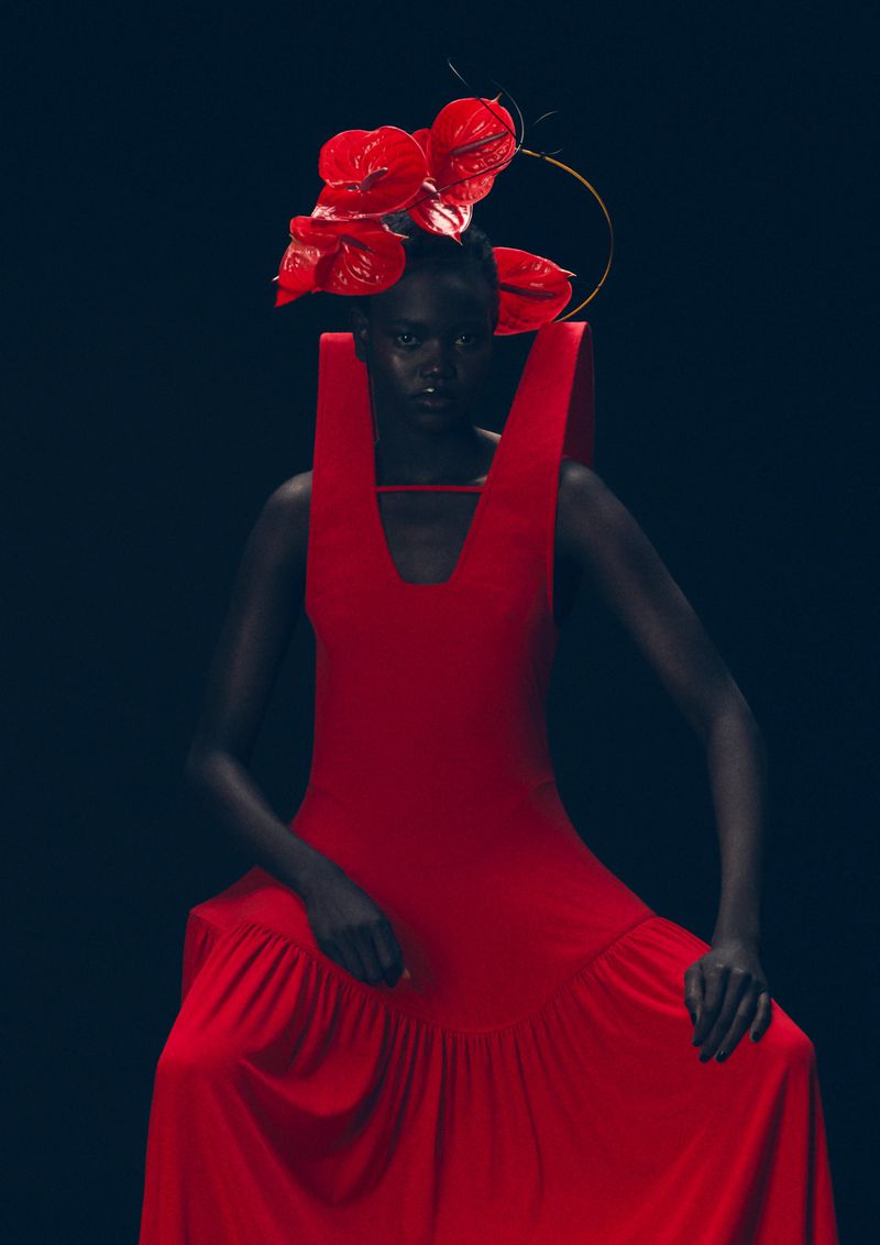 Elegant woman in a red dress and floral headpiece against a dark background, fashion photography, showcasing texture and form.