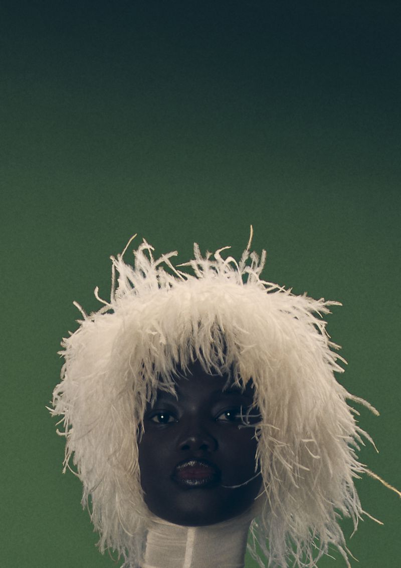 Close-up portrait of a black woman with a white feathered headpiece against a green background. Fashion and beauty photography.