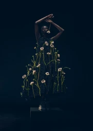 Model wearing a dark dress adorned with white flowers against a black background for L'Officiel Austria