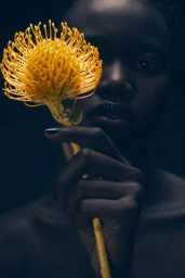 Model holding a vibrant yellow pincushion flower in front of her face in a moody portrait for L'Officiel Austria
