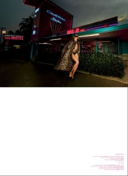 Model posing in a leopard print cape and sunglasses outside a diner with glowing neon signage at dusk.