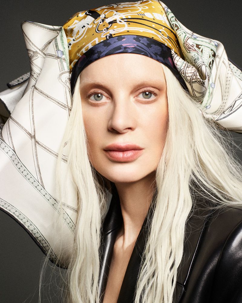 Close-up portrait of Kristen McMenamy wearing an elaborate printed silk headscarf and dark leather jacket for W Magazine