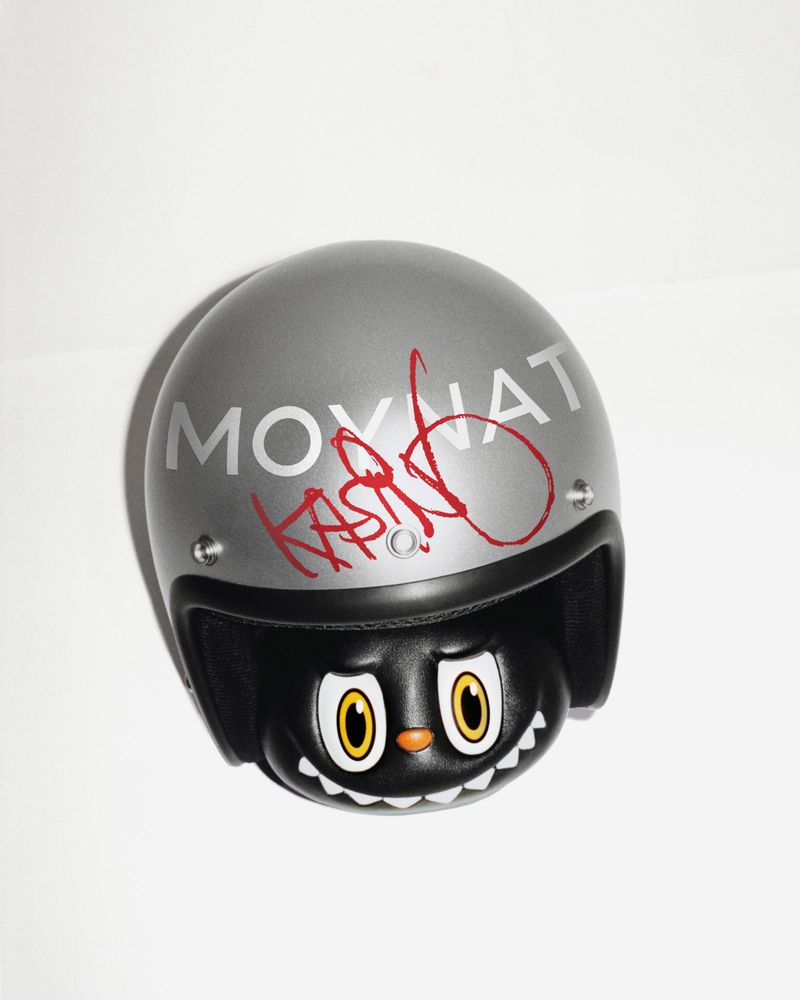 Silver Moynat helmet signed in red marker by Kasing Lung over a black character figurine on a white background.