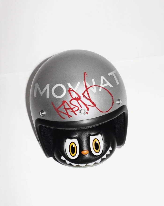 Silver Moynat helmet signed in red marker by Kasing Lung over a black character figurine on a white background.
