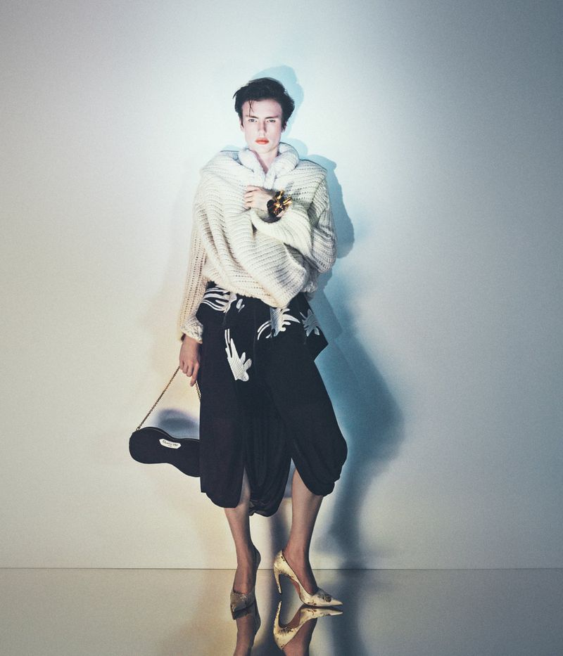 Model Charlie Jones in a chunky cream knit wrap, printed black skirt, and pointed heels against a studio backdrop.