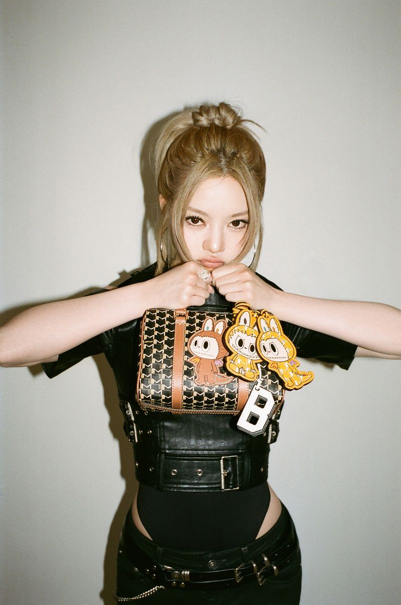 Soo Joo Park holds a patterned Moynat handbag with Kasing Lung charms in a studio portrait against a plain backdrop.