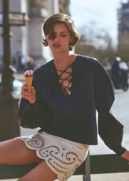 Model Valerie Scherzinger holding an ice cream cone wearing a navy lace-up blouse and white cutout mini skirt outdoors.