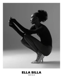 Black model crouching in profile wearing a dark bodysuit and metallic heels against a grey seamless background