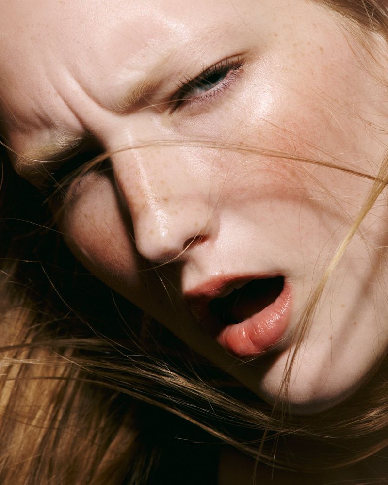 Close-up portrait of a light-skinned woman with blonde hair, looking at the camera with an open mouth and furrowed brow.