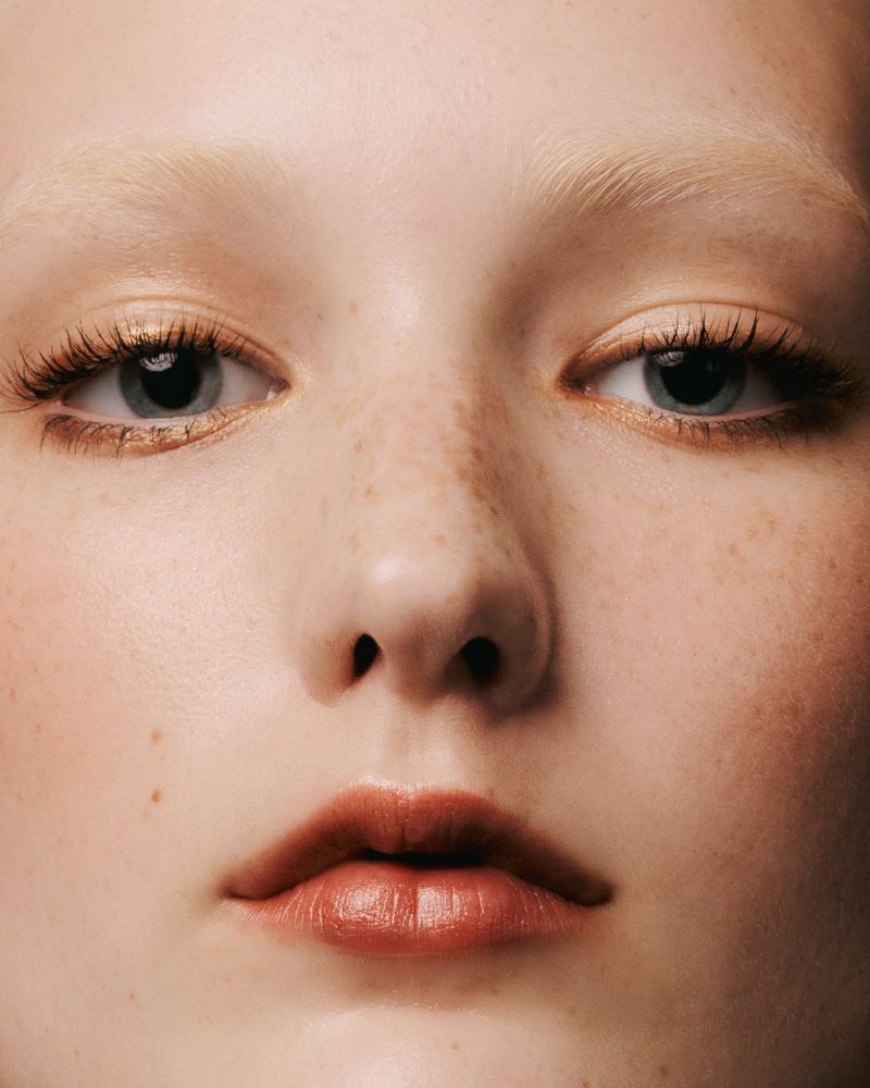 Close-up portrait of a young fair-skinned female with light hair, freckles, and blue eyes. Beauty shot showcasing natural makeup.