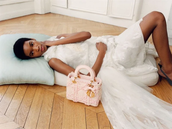 Model lying on parquet floor with a pink tweed handbag and a pale blue cushion for Dior womens fall 2026