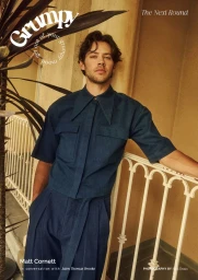 Actor Matt Cornett poses in a matching navy blue short-sleeve shirt and pleated trousers on a balcony for Grumpy Magazine.
