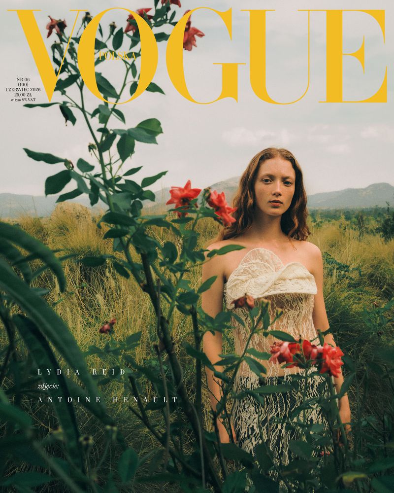 Model Lydia Reid standing in a grassy meadow behind blooming red roses on the cover of Vogue Polska.