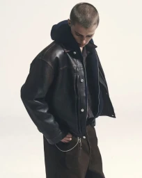 Model Elias Monstrey wearing an oversized black leather jacket and dark hoodie against a white studio background.
