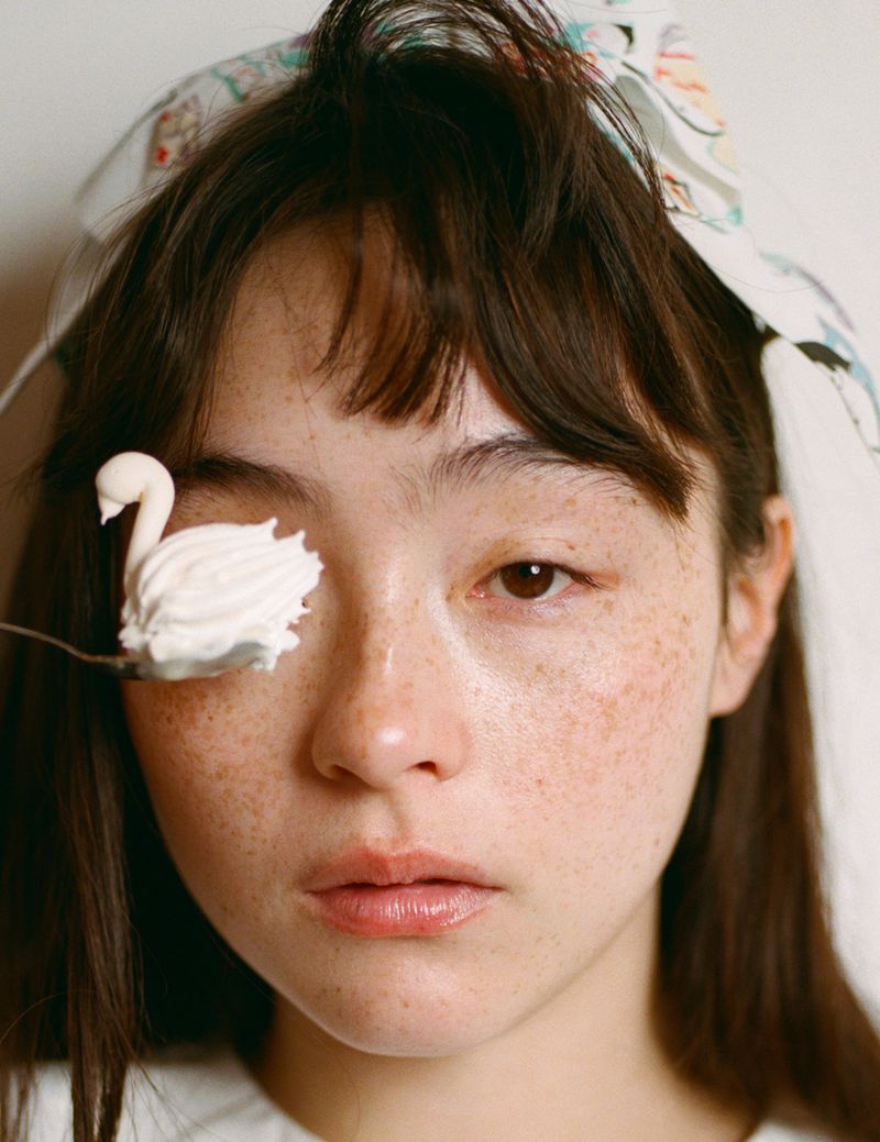 Close-up portrait of Serena Motola holding a swan-shaped whipped cream dollop over her eye for Ashley Williams.