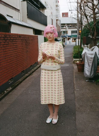 Serena Motola with a pink bob hairstyle wearing a patterned cream midi dress set on an urban street for Ashley Williams.